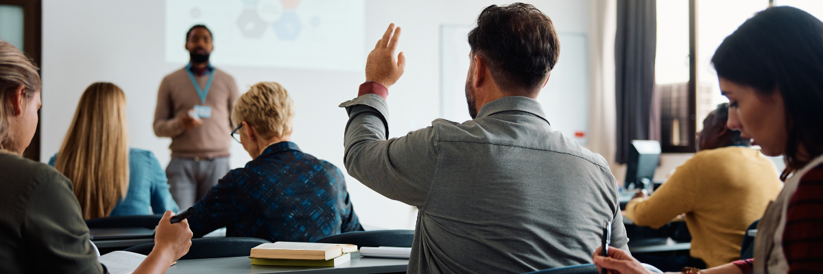 Adults in a classroom and one has their hand raised