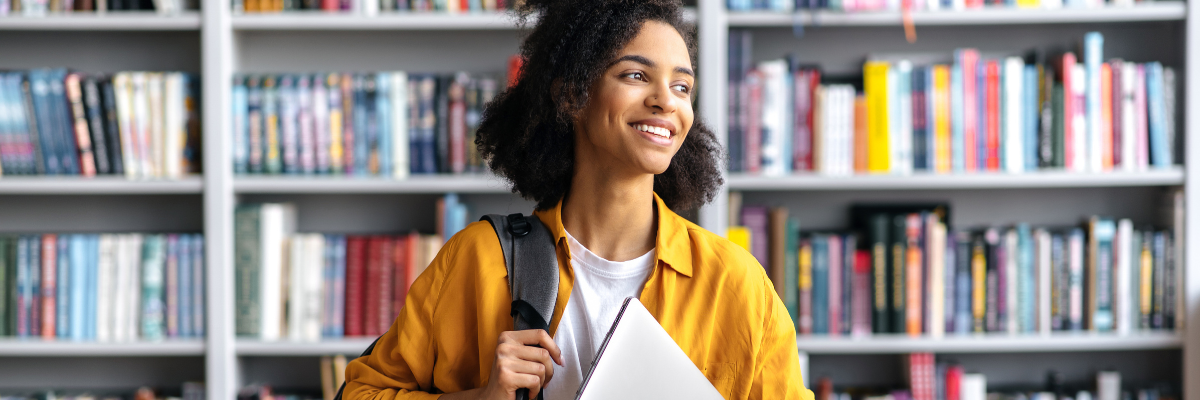 Student carrying laptop and smiling in the library